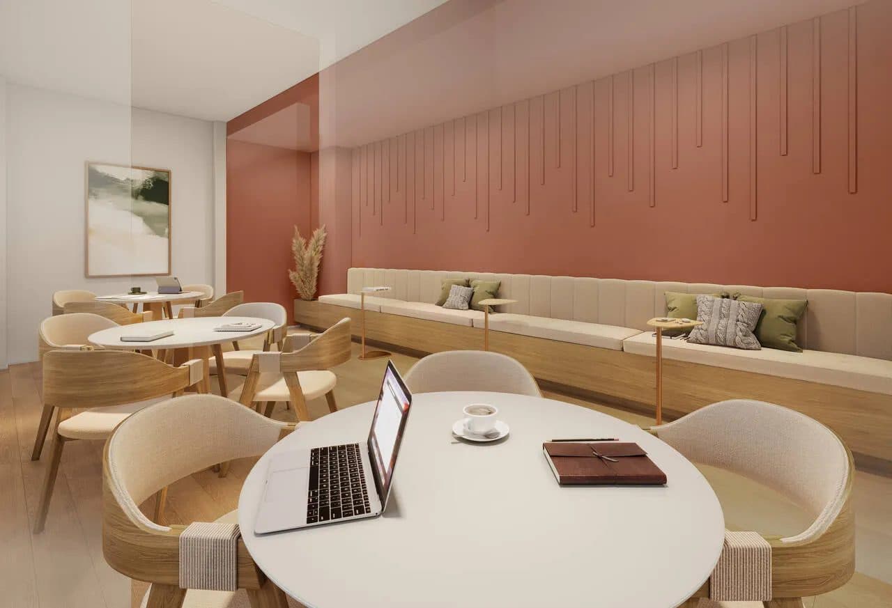 Sala de estudos ou coworking com mesas redondas, cadeiras e longas bancadas encostadas na parede.